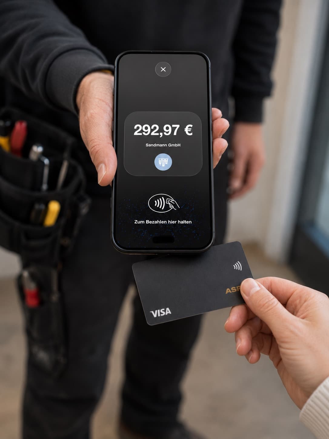 Handwerker hält sein Smartphone hin, der Kunde zahlt mit der Karte per Tap to Pay