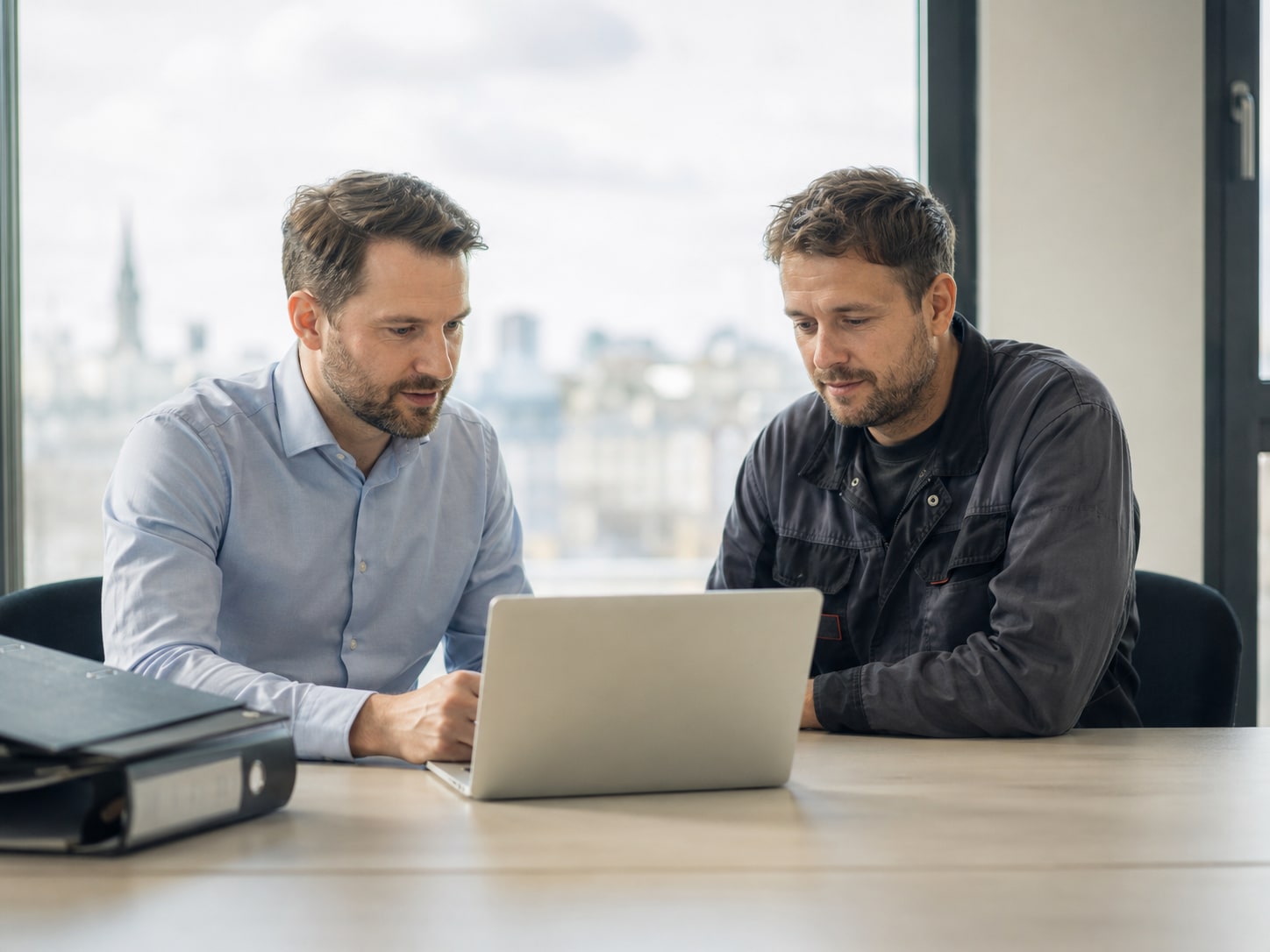 Steuerberater und Handwerksmeister schauen gemeinsam auf die Buchhaltung am Laptop